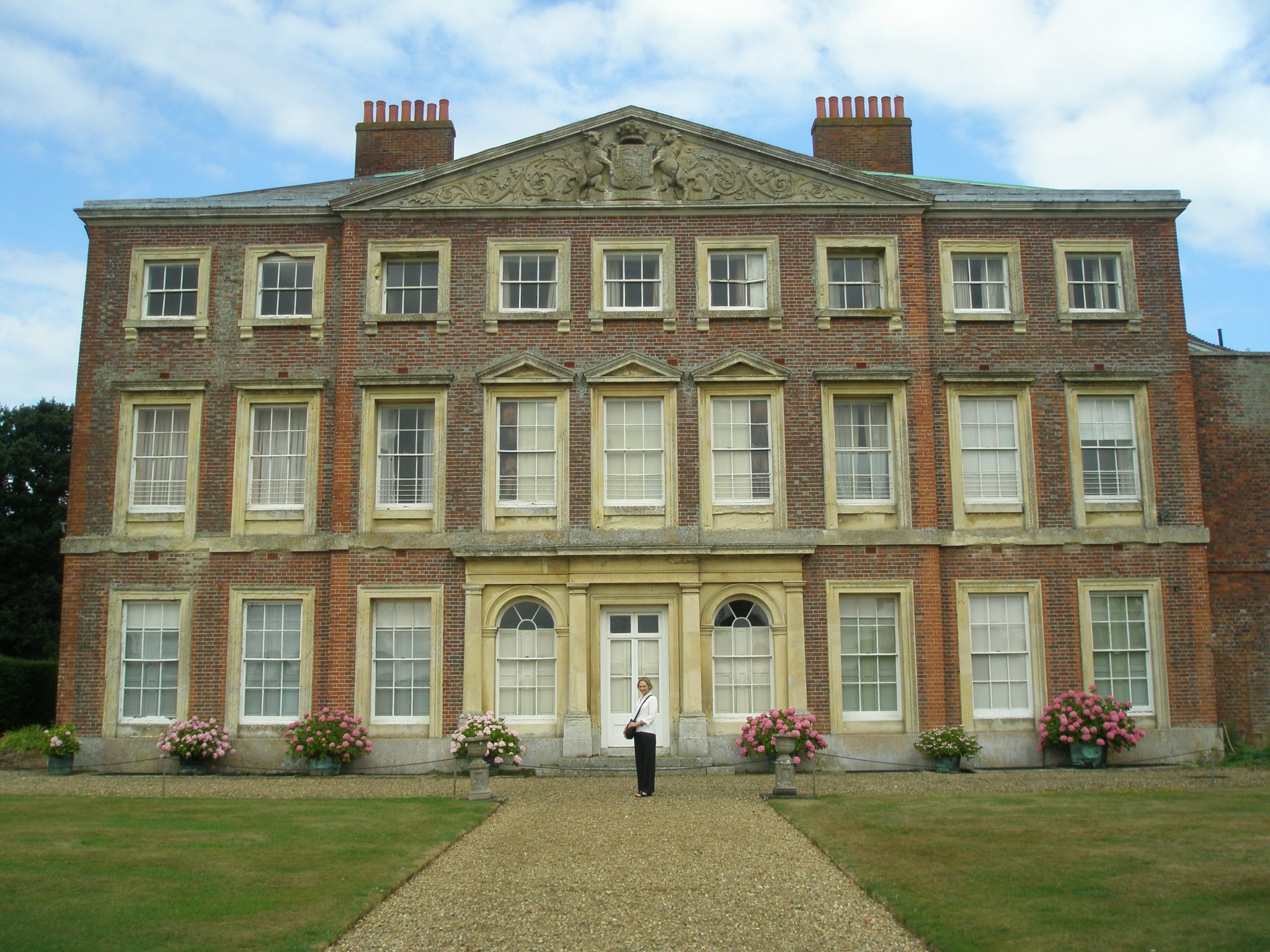 The House at Goodnestone Park, near Canterbury. Nan provides human scale here, in front of the manor, which was built for Mister Brook Bridges, in 1700. Goodnestone (pronounced GUN-Stone) Park is famous because of its link to Jane Austen. In 1791, Elizabeth (daughter of Sir Brook Bridges, 3rd Baronet) married Edward Austen, a brother of Jane Austen. During the early years of their marriage, Elizabeth and Edward Austen lived at Rowling, a manor house close to Goodnestone Park, where Elizabeth's parents resided. Jane Austen was a frequent visitor, and made many references to Goodnestone Park in her letters. This photo was taken on August 8, 2013.